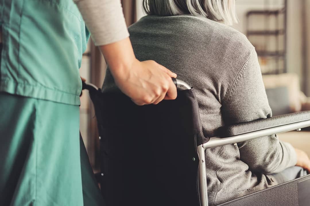 A home care nurse assisting an elderly patient in a wheelchair.